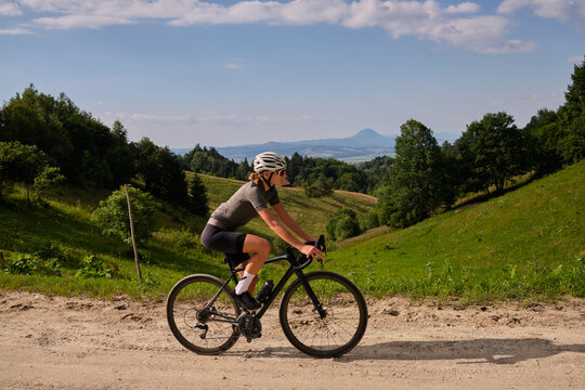 Female cyclist riding a gravel bike on a gravel road with a view of the mountains. Athlete is wearing cycling kit.