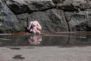 Lonely and lost plush rabbit sitting by a stone wall.