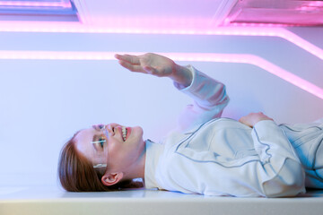 Woman in futuristic costume. Female in modern VR glasses interacting with network while having virtual reality experience. Augmented reality game, future technology, AI concept. VR. Neon blue light.