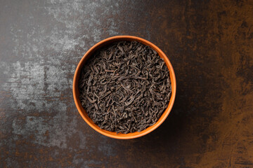 Dry black tea in a bowl on a dark background