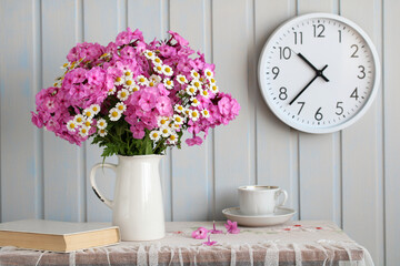A bouquet of pink phlox and daisies in a white jug. Still life with flowers and clocks.