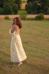 Fototapeta na wymiar A young lady walks barefoot in a field at sunset