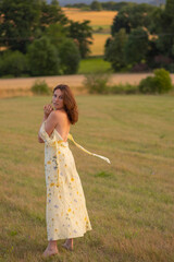 Fototapeta na wymiar A young lady walks barefoot in a field at sunset