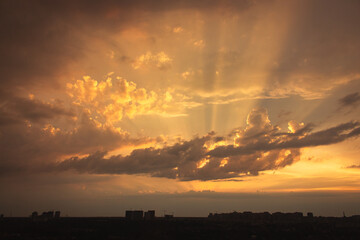 Dramatic evening sky with rays of light over city. Aerial view above cityscape in the dusk. Heaven concept. Sunshine in the sky. Sunset scenic sky. Sun rays through the clouds.