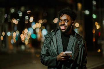Portrait of a happy urban man standing on the street and having a phone call at night.
