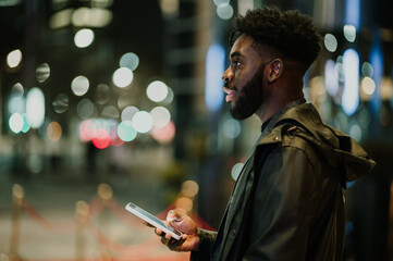 Profile view of an urban African American man using a phone on a street at night.