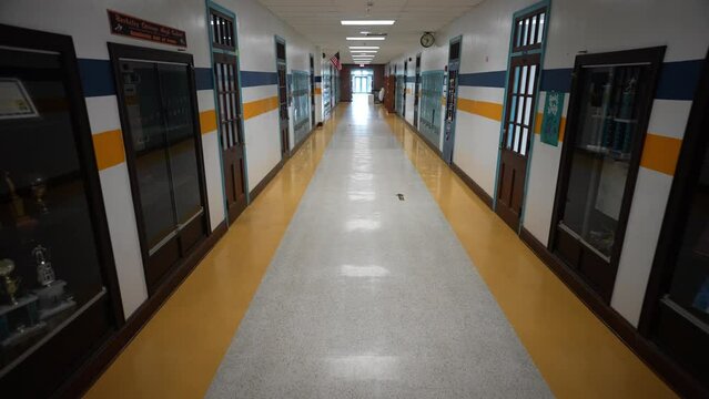 High angle slow motion push in down a long empty high school corridor hallway with US American flag.