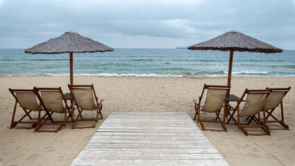 Empty wooden sunbeds and sun umbrellas on deserted beach on cold cloudy day. End of seasonal tourism, travel in winter.