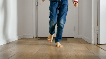 Little boy's feet as he runs down the long wooden corridor of his home. Happy childhood, indoor...