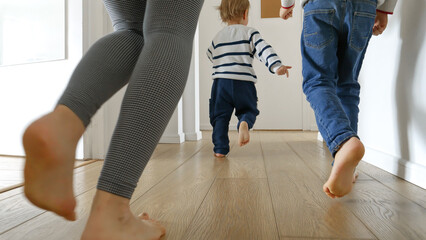 Closeup of mother and two boys running on the wooden floor at home. Concept of family love, joy,...
