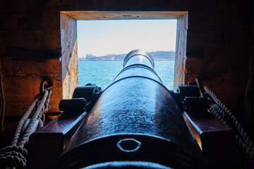 Sea view out of a gunport in hull of the ship over the gun cannon muzzle in on the gun deck of a...