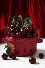 Ripe cherries in a red bowl on a white wooden surface. Delicious juicy berries