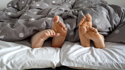 Closeup of man and woman's feet lying on a soft bed and gently touching each other. Concept of love, affection, and intimacy at home.