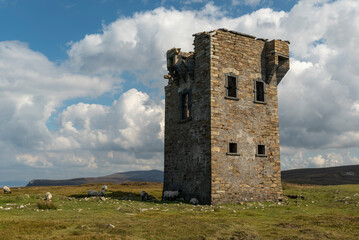 Flock of sheep grazing around the Glencolumbkille signal tower under a dramatic cloudy sky, County Donegal, Ireland