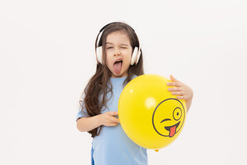 A child girl hides his face behind a yellow winking emoticon on white background. Funny face. World Emoji Day