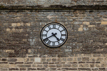 Vintage stone wall with real clock, white dial, black sword-shaped hands, Roman numerals. Weathered texture, time reads 4:40. Timepiece, classic design, historic, antique