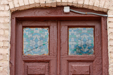 An old antique wooden door with small windows decorated with colorful mosaics. Painted wooden door on an old brick house.