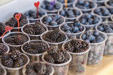 A lot of blackberries and blueberries in plastic glasses for the sale. Fresh berries in takeaway cups on the market counter.