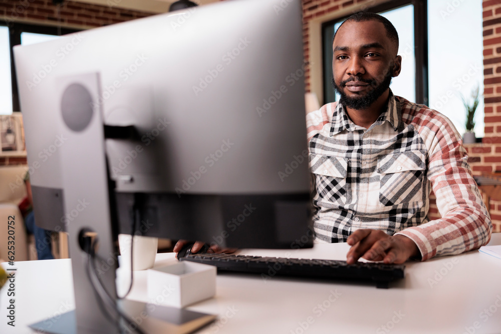 Poster confident african american programmer looking at computer screen and typing while working remote fro