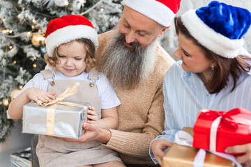 Grandmother, grandfather, daughter and granddaughter celebrating holidays at home together. Happy smiling family near beautiful Christmas new year tree exchanging gifts in the morning