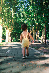 Toddler in suspenders walking through an urban park on a hot summer afternoon.