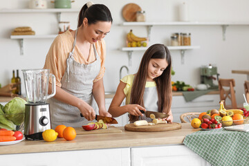 Little girl with her mother cutting banana for smoothie in kitchen