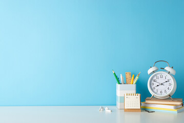 Engage your audience with side view image of a student's efficient workspace, consisting of a white desk, alarm clock, notepads and stationary on a blue background, allowing for text or advertisements - Powered by Adobe