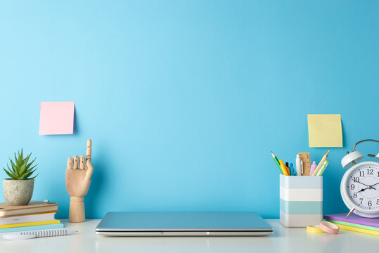 The Desk Of A Student During Online Education, Captured From The Side, Featuring A White Desk, Laptop, And Stationery On An Isolated Blue Background, Offering Space For Text Or Advertising