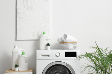 Washing machine with bottles of detergent and houseplant near white wall