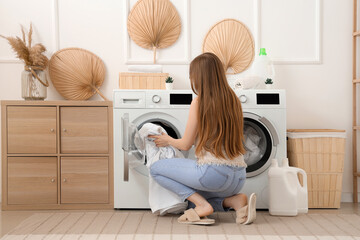Woman putting dirty clothes into washing machine in laundry room