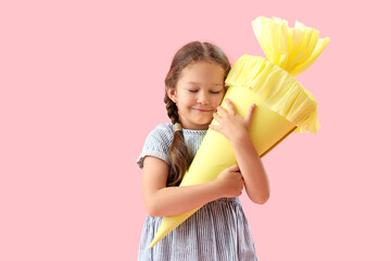Happy little girl with yellow school cone on pink background