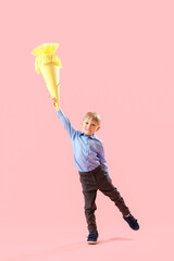 Happy little boy with yellow school cone jumping on pink background