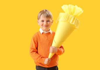 Happy little boy with school cone on yellow background