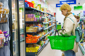 A young girl with a grocery basket in her hands walks around the store. The blonde girl chooses food. The concept of healthy eating. The era of consumption.
