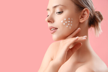 Pretty young woman with cream on her face against pink background