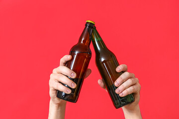 Fototapeta premium Male hands with bottles of cold beer clinking on red background