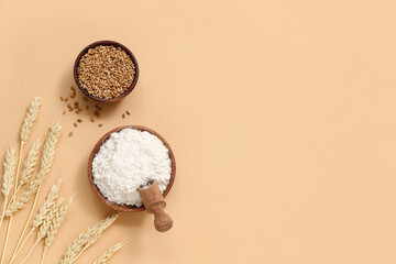 Bowls with wheat flour and grains on beige background
