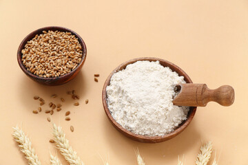 Bowls with wheat flour and grains on beige background