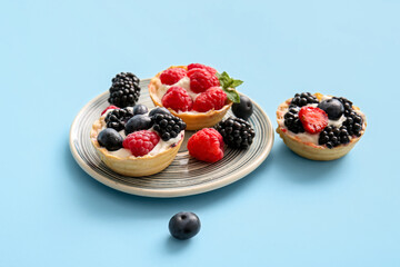 Plate of tasty tartlets with whipped cream and berries on blue background