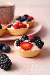 Tasty tartlets with whipped cream and berries on pink tile background