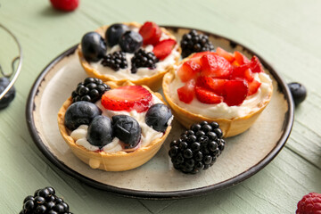 Plate of tasty tartlets with whipped cream and berries on green wooden background