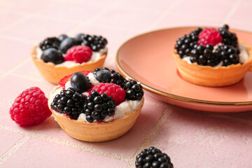 Tasty tartlets with whipped cream and berries pink tile background