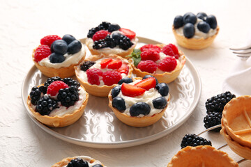 Plate of tasty tartlets with whipped cream and berries on white background