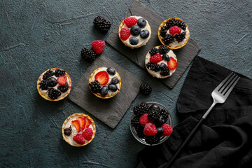 Fototapeta na wymiar Tasty tartlets with whipped cream and berries on dark background