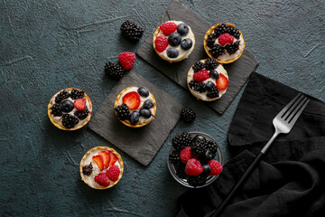 Tasty tartlets with whipped cream and berries on dark background