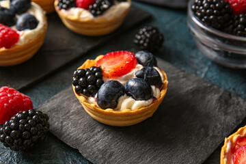 Tasty tartlets with whipped cream and berries on dark background