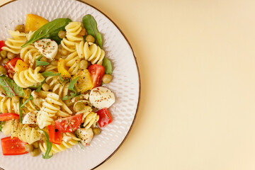 Plate of tasty pasta salad with pepper and peas on yellow background
