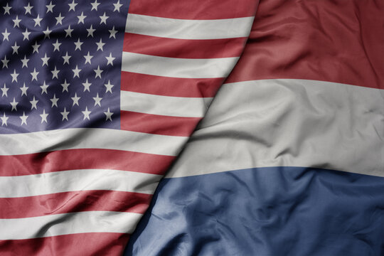 big waving colorful flag of united states of america and national flag of netherlands .