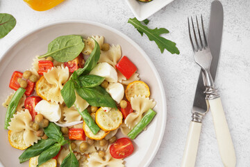 Plate of tasty pasta salad with peas and basil on white background