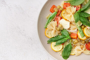Plate of tasty pasta salad with peas and basil on white background
